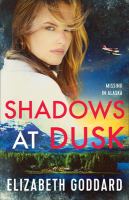 Cover of Shadows at Dusk. Woman stares at camera, hair blowing a bit in the wind, looks serious, title below her, bottom is scenery from Alaska with mountains and green trees and a lake.