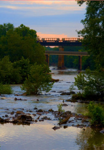 a view of the river from Red Slide Park at sunset with train cars on the tracks on the bridge over the river