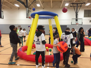 athletes and students playing with inflatable basketball goal