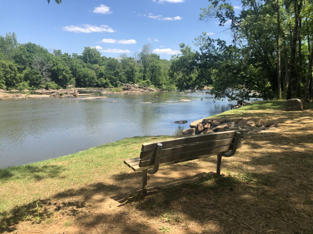 A park bench sits in front of a view of the Haw River at Swepsonville River Park
