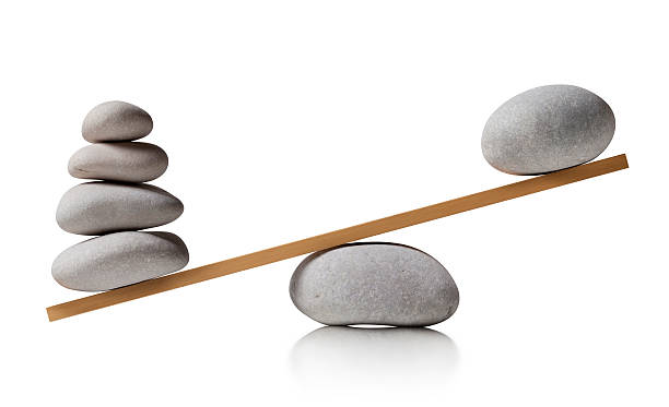 A balance board sitting on a rock, tilted left with four stones on the low left end and one stone on the high right end